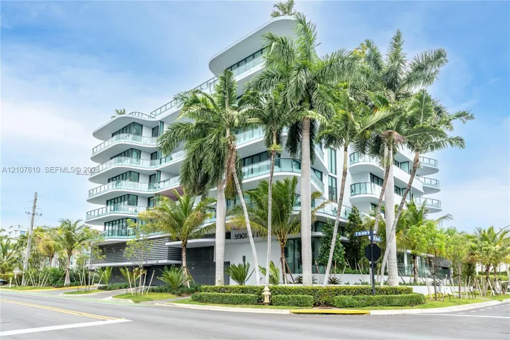 Modern architectural building featuring multi-level curved terraces, glass balcony railings, floor-to-ceiling windows, and mature palm landscaping
