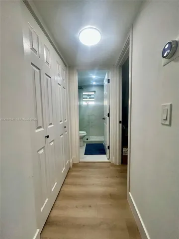 Hallway featuring wood-finish flooring, white panel-style closet doors with matte black hardware, and a flush-mount ceiling light fixture