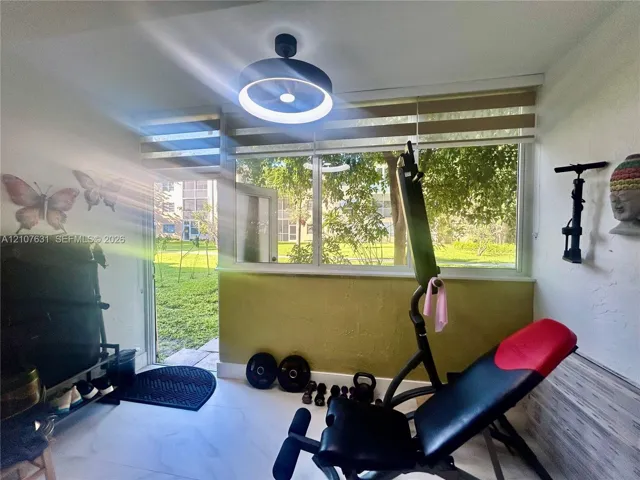 Large window with horizontal blinds, modern circular LED ceiling fixture, neutral tile flooring, and exterior access door