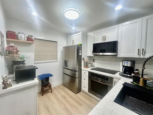 Kitchen featuring white shaker-style cabinetry, stainless steel appliances, light-toned stone-finish countertops, wood-finish flooring, and a black undermount sink with a gooseneck faucet