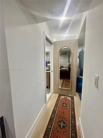 Hallway featuring wood-finish flooring and a built-in wood-panel wall section with a recessed arched mirror