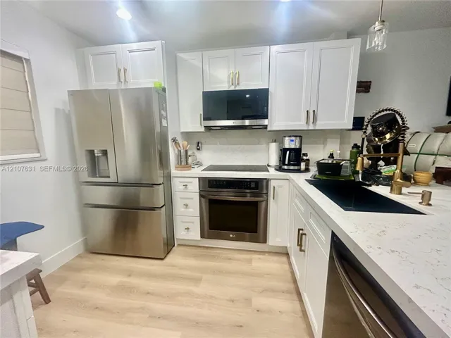 Kitchen featuring white shaker-style cabinetry, quartz countertops, wood-finish flooring, and stainless steel appliances