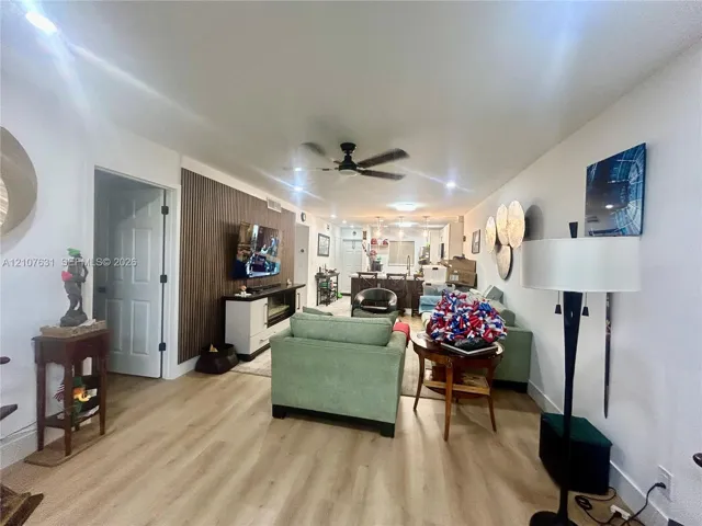 Open-concept living space featuring wood-finish flooring, vertical slat wood-tone accent wall, recessed lighting, and a ceiling fan