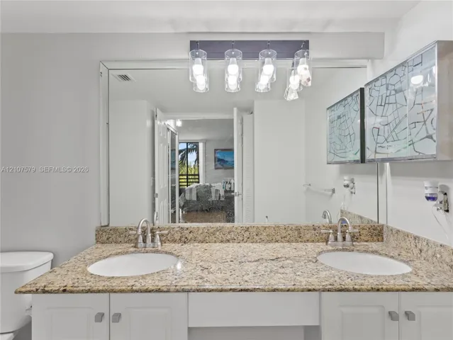 Dual-sink vanity with stone countertop, white cabinetry, large wall-mounted mirror, and multi-bulb decorative light fixture