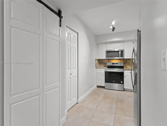 Kitchen featuring white shaker-style cabinetry, stone-surface countertops, stainless steel appliances, tile flooring, and a white sliding barn door