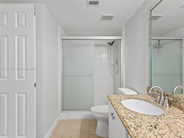 Bathroom featuring stone-finish countertop with an undermount oval sink, sliding glass shower enclosure, white cabinetry, and tile flooring