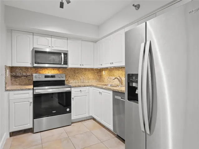 Kitchen featuring white cabinetry, stone countertops, tiled flooring, and stainless steel appliances including a refrigerator, dishwasher, range, and built-in microwave