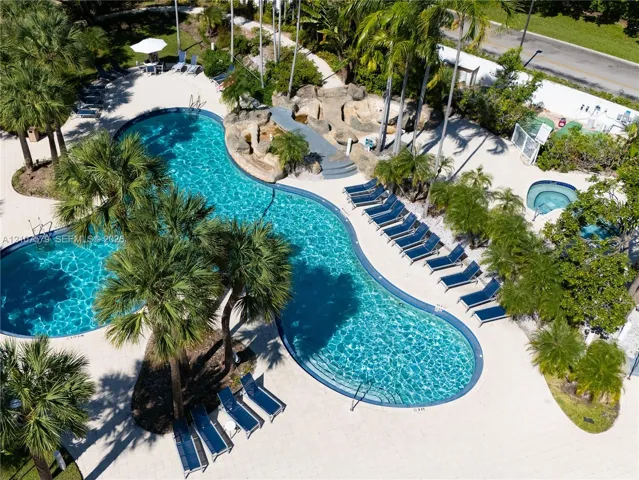 Curvilinear swimming pool with integrated rock waterfall feature, tiled patio decking, and separate elevated spa, surrounded by mature palm trees