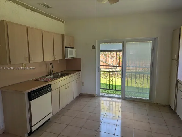 Kitchen featuring light-toned cabinetry, dual-basin stainless steel sink with high-arc faucet, integrated dishwasher, and tiled flooring with sliding glass door access to the exterior