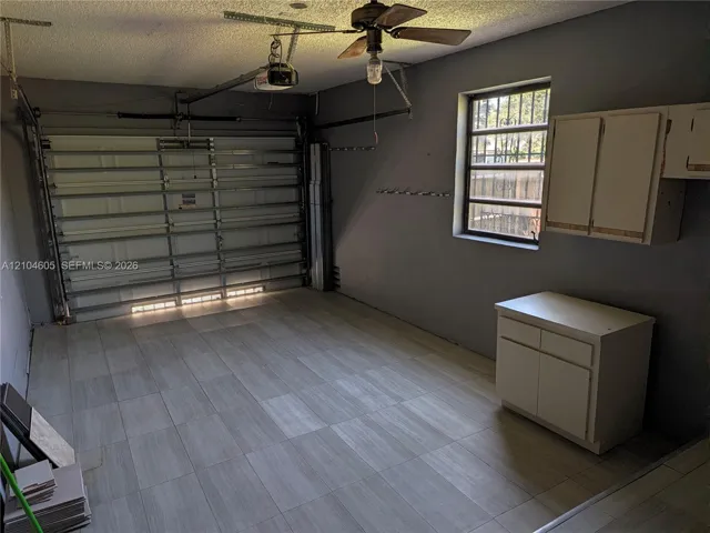 Garage featuring tile flooring, metal sectional garage door, built-in wall and base cabinetry, and ceiling-mounted paddle fan
