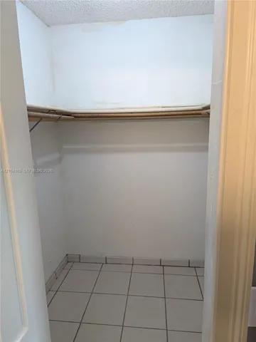 Storage closet featuring tile flooring, a built-in overhead shelf, and a support rod