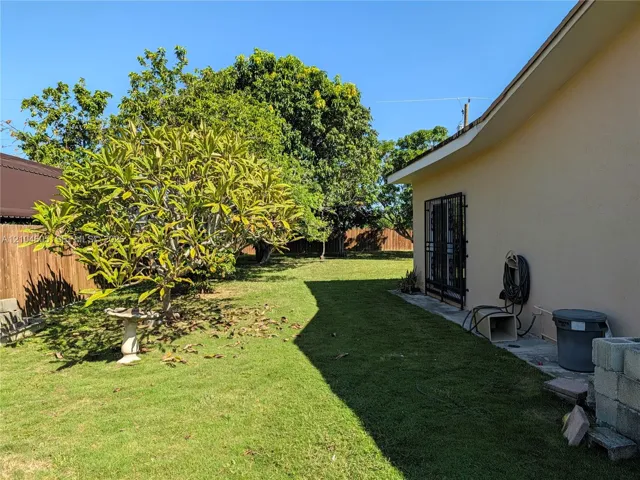 Expansive backyard featuring a grass lawn, mature trees, wood privacy fencing, and a concrete side patio