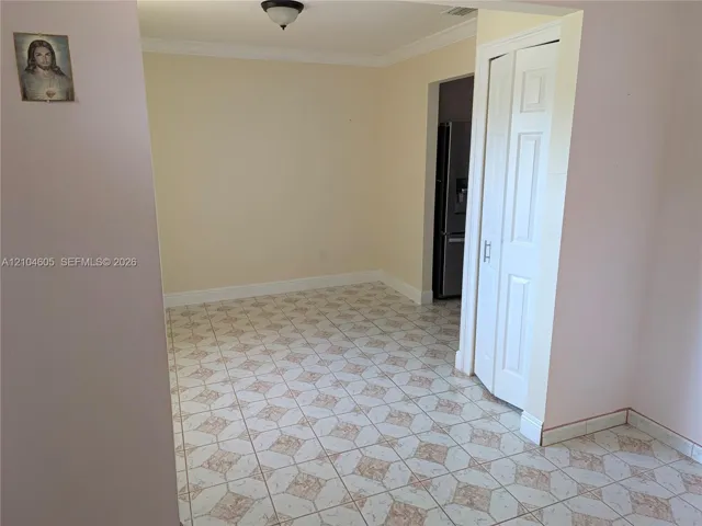 Neutral-toned interior space featuring geometric patterned tile flooring, crown molding, and a bi-fold closet door with brushed nickel hardware