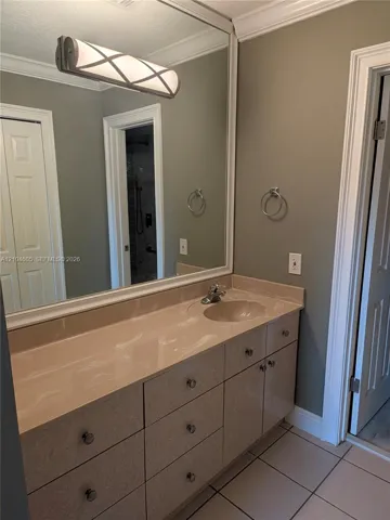 Vanity featuring integrated countertop and sink, multi-drawer cabinetry with metal hardware, framed wall-to-wall mirror, decorative linear light fixture, and tile flooring