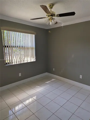 Neutral-toned interior space featuring light-colored tile flooring, crown molding, vertical window blinds, and a ceiling-mounted fan with integrated lighting