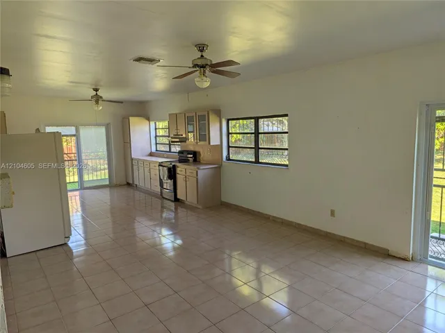 Open-concept kitchen featuring ceramic tile flooring, neutral cabinetry, dual ceiling fans, and two sliding glass exterior doors