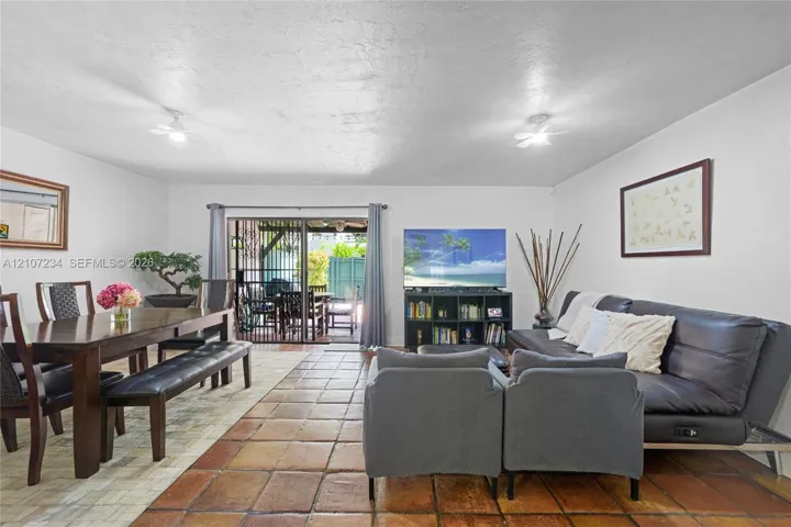 Open-concept living space featuring large-format ceramic tile flooring, dual ceiling-mounted lighting fixtures, and sliding glass doors providing access to the rear exterior