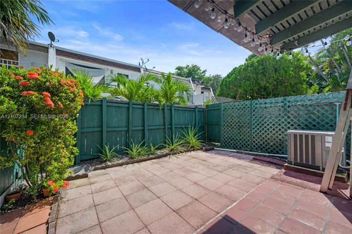 Private patio featuring terracotta-style paving, emerald-green wood privacy fencing, decorative lattice screening, and established tropical landscaping