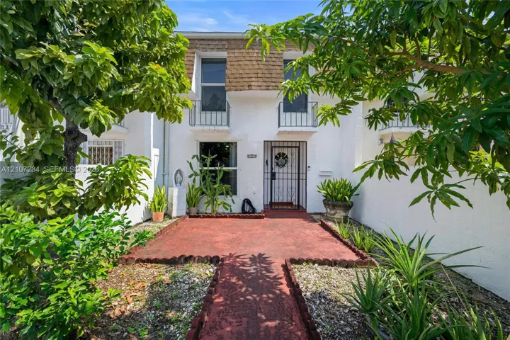 Exterior facade featuring white stucco finish, second-story decorative iron balcony railings, a metal security door, and a painted masonry walkway