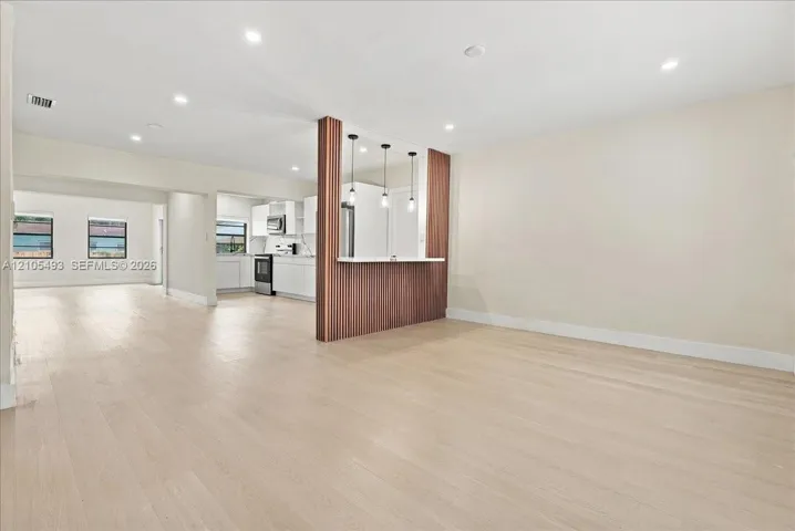 Open floor plan featuring wood-finish flooring, a wood-paneled peninsula with integrated counter seating, recessed lighting, and three pendant lights