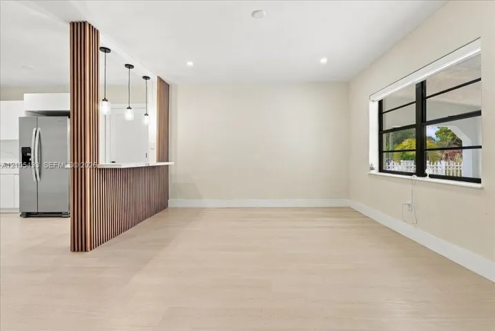 Wood-finish flooring, custom vertical slat wood-finish partition wall, built-in breakfast bar with quartz countertop, pendant lighting, and horizontal multi-pane windows with black framing