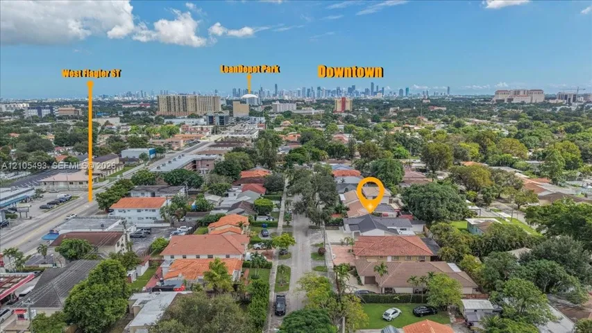 Aerial perspective showcasing a residential lot with a tile-roof structure and mature trees, positioned in an urban environment with an expansive metropolitan skyline background