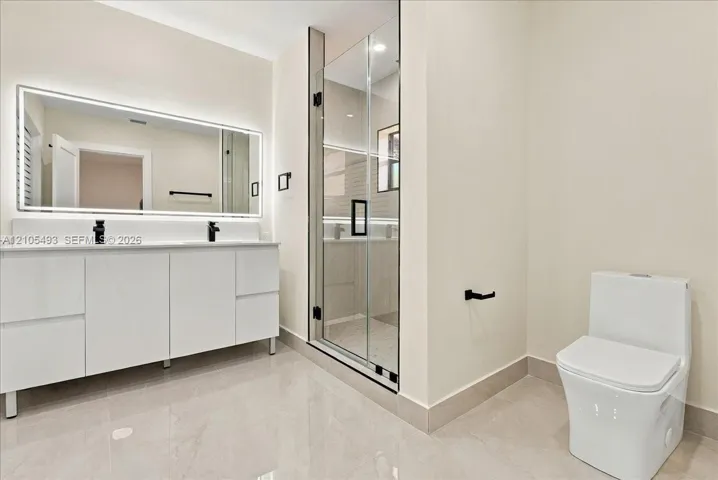 Floating double vanity with integrated sinks, LED-backlit mirror, glass-enclosed shower, and matte black fixtures