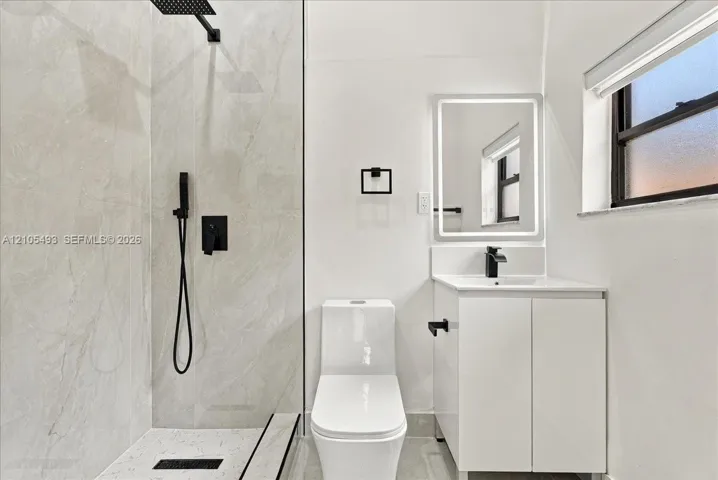 Bathroom featuring a glass-enclosed shower with matte black fixtures, rainfall showerhead, and floor-to-ceiling tile surround