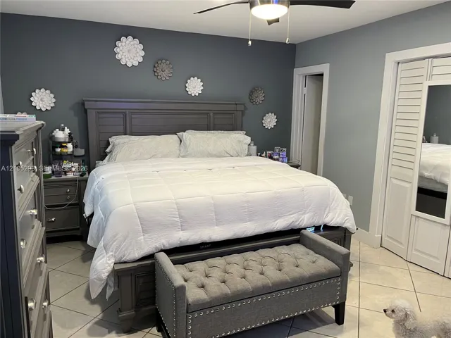 Large-format tile flooring, louvered closet doors with integrated mirror, and a ceiling-mounted light fixture with fan