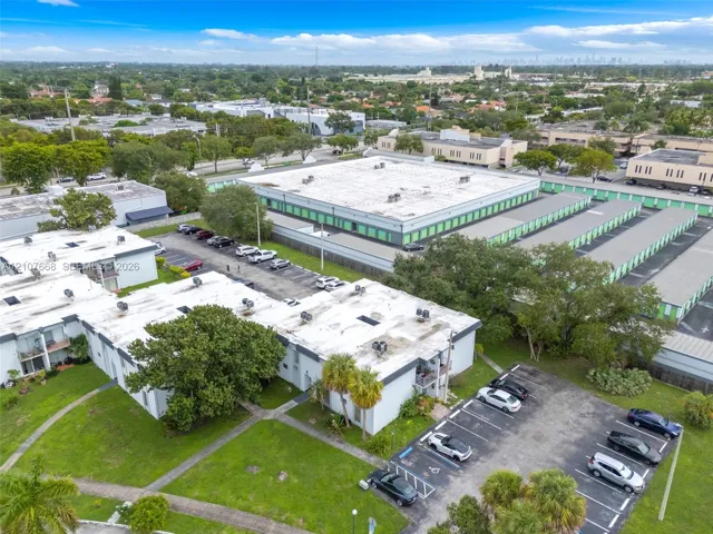 Aerial perspective of multi-unit residential buildings featuring white exterior finishes, dedicated asphalt parking lots, manicured green space, and mature palm trees
