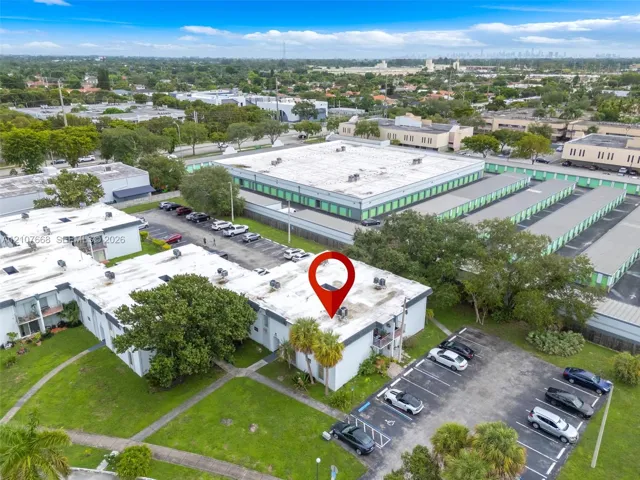 Aerial perspective of a multi-unit property featuring flat roofing, dedicated asphalt parking, integrated exterior lighting, and landscaped green space