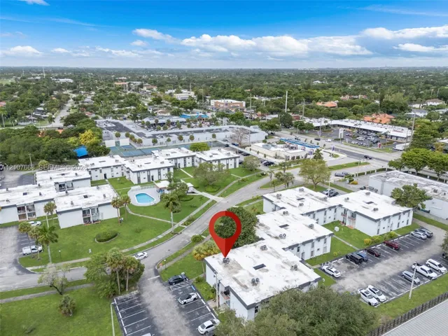 Aerial perspective of multi-family complex featuring paved parking areas, sprawling grass lawns, and an outdoor swimming pool