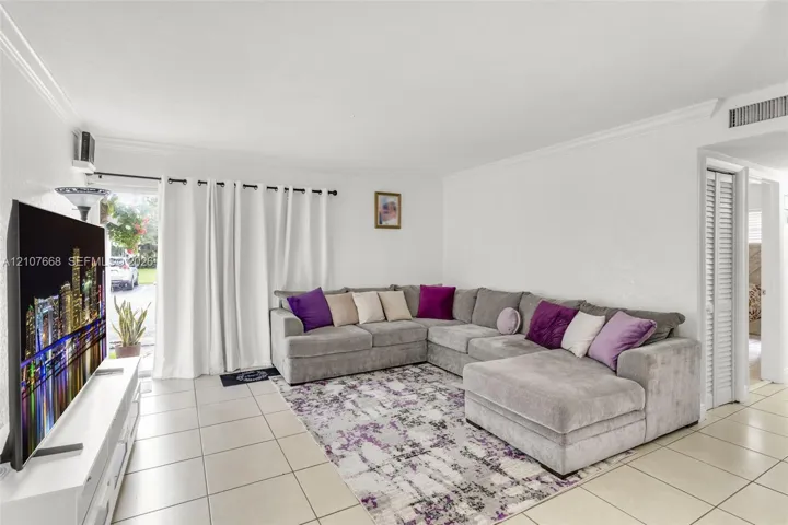 Living space featuring neutral ceramic tile flooring, crown molding, and louvered closet doors