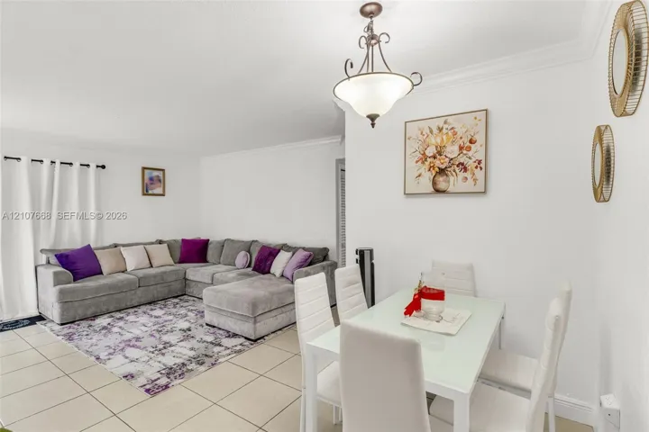 Open living area featuring large-format tile flooring, crown molding, and a tiered metal chandelier with frosted glass shades