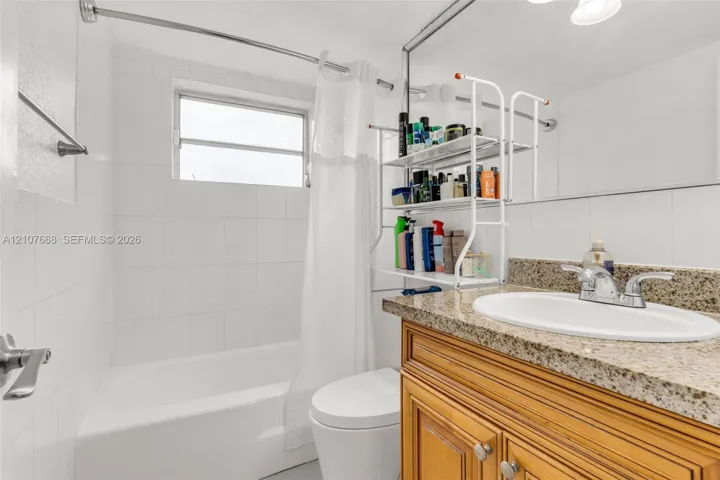 Bathroom featuring a wood-finish vanity with a stone-composite countertop, integrated oval basin, white wall tile surround, and an oversized vanity mirror