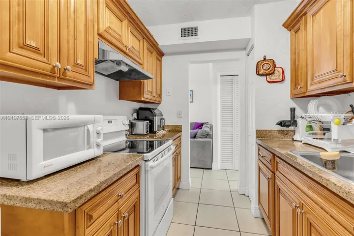 Kitchen featuring shaker-style wood cabinetry, stone-finish countertops, tile flooring, and integrated white appliances