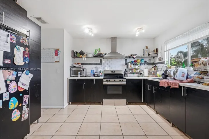 Kitchen featuring dark cabinetry, stainless steel range with overhead vent hood, white subway tile backsplash, and ceramic tile flooring