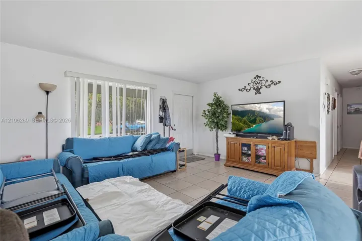 Living area featuring neutral tile flooring, expansive window with vertical blinds, and a solid-core entry door