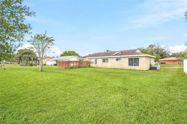 Expansive backyard featuring a large grass lawn, mature trees, and a textured exterior finish