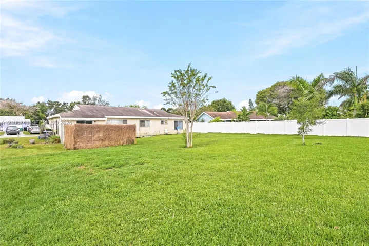 Expansive backyard featuring a large grass lawn, mature trees, and a full-perimeter white vinyl privacy fence