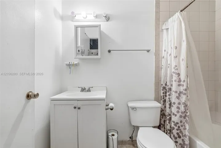 Bathroom featuring a white vanity with integrated basin, wall-mounted medicine cabinet, multi-bulb vanity light, and a tiled tub surround