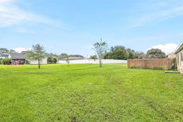 Expansive backyard featuring a manicured lawn, perimeter fencing, and mature trees