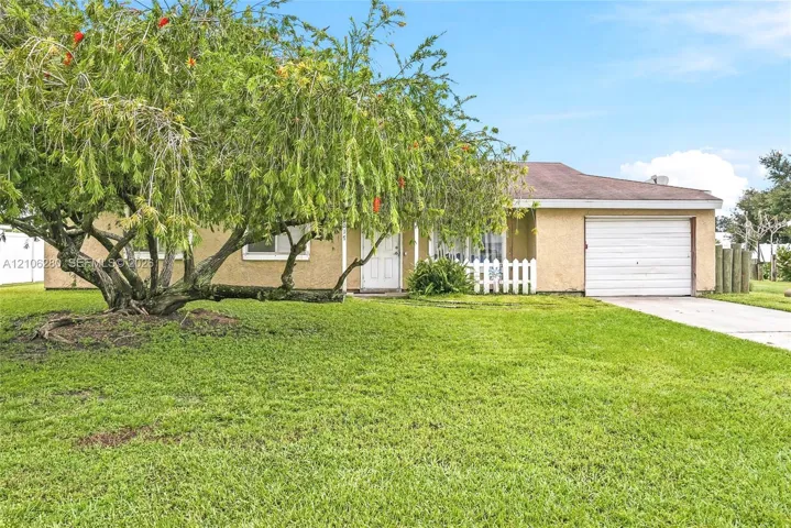 Stucco exterior featuring a concrete driveway, attached one-car garage, and picket fencing