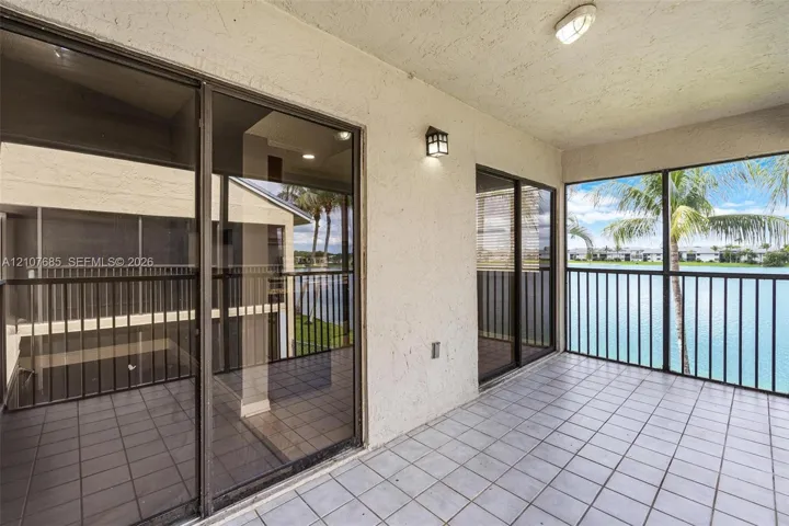 Covered balcony featuring tile flooring, sliding glass doors, screen enclosure, and metal railings overlooking the water