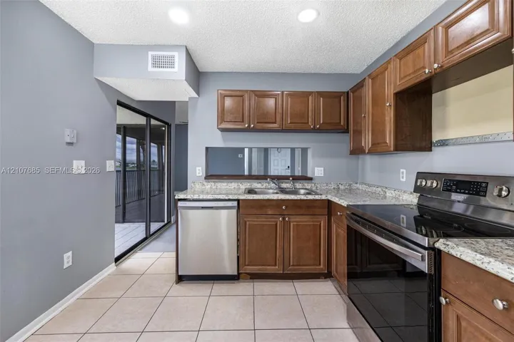 Kitchen featuring medium-tone wood cabinetry, stone-patterned countertops, stainless steel appliances, recessed ceiling lighting, and ceramic tile flooring