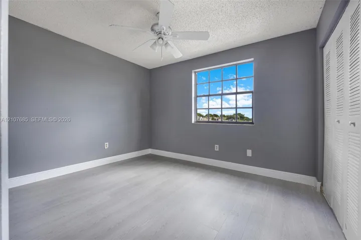 Room featuring gray walls, wood-finish flooring, a multi-pane window, a ceiling fan, and louvered bifold closet doors