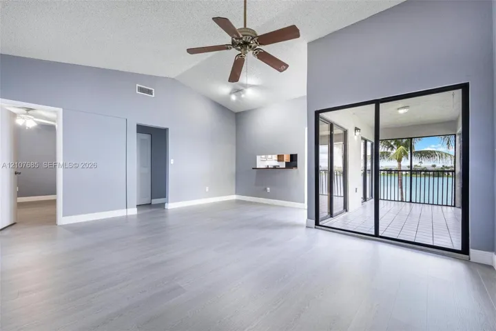 Vaulted ceilings, wood-finish flooring, ceiling fan, and floor-to-ceiling sliding glass doors leading to a screened lanai with water scenery