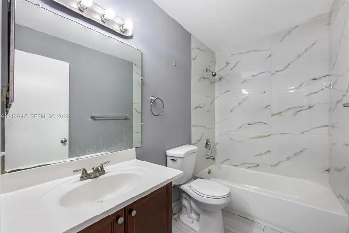 Bathroom featuring a vanity with an integrated sink, large wall-mounted mirror, light fixture with globe shades, and a shower-tub combination finished with floor-to-ceiling stone-look tile