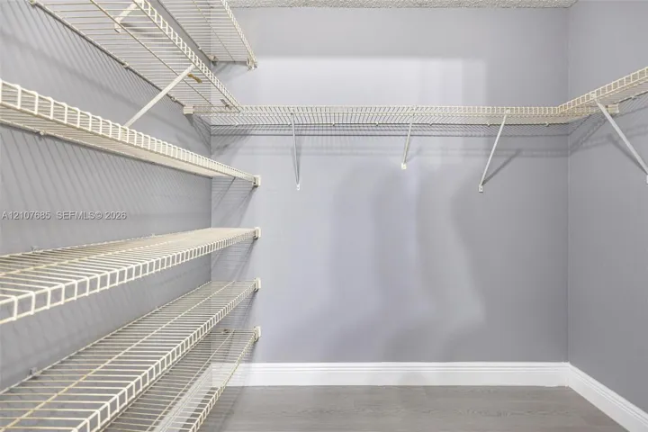 Walk-in storage space featuring multi-tiered white wire shelving, neutral-toned walls, and wood-finish flooring