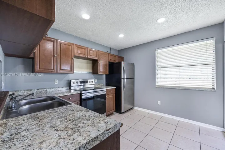 Kitchen featuring wood cabinetry, stone-finish countertops, dual-basin stainless steel sink, stainless steel range, and tile flooring